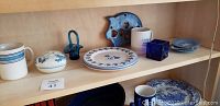 Close-up of blue, white, and cobalt décor items arranged on a bookshelf, including Spode dishes with puffins print, blue glass, and ceramic pieces.