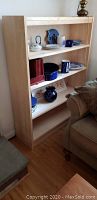 Wooden bookshelf with three shelves, holding decorative items such as ceramic pieces, glassware, and books.