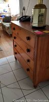 Side angled view of the antique wooden four-drawer dresser showing the wood grain and rounded legs with some items on top.