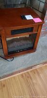 Wooden Allen brand electric heater with glass front and faux logs inside, placed on the floor.