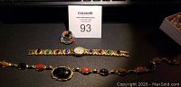 Photo showing Lucoral watch bracelet, scarab beetle pin, and necklace with oval cabochon stones and scarab centerpiece on dark surface