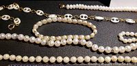 Close-up photo showing pearl necklaces and a bracelet with white enamel or resin chain links and gold-tone metal on a black surface.