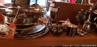 Photo showing multiple silver plated trays stacked together, a silverware basket, lidded sugar bowl or tea caddy, small pitchers, and bowls in vintage condition with tarnish.