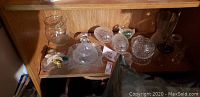 Glassware collection displayed on shelf, includes clear glass bowls, jars with lids, and small items.
