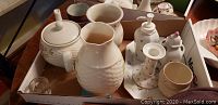 Box containing multiple porcelain items, including two Belleek pieces: a teapot and creamer with floral designs