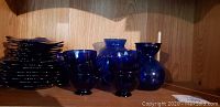 Shelf with stacked cobalt blue salad plates and multiple cobalt blue glass vases and cups arranged in front