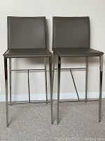 Front view of two grey recycled leather stools with stainless steel legs against wall