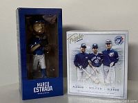 Front view of two unopened Toronto Blue Jays bobblehead boxes: one single Marco Estrada bobblehead and one triple bobblehead featuring Alomar, Molitor, Olerud