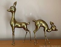 Two brass deer sculptures side by side on wood surface against neutral background