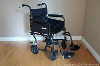 Three-quarter front view of chair showing black aluminum frame, nylon seat, swing-away footrests and front casters