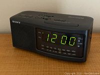 Front and side view showing the Sony digital alarm clock radio with the time displayed in green LED digits 12:00.