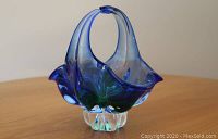 Front and side view showing the blue and green blown glass basket bowl with curved handle and clear base.