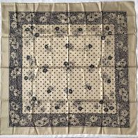 Flat laid beige silk scarf with black floral and dot pattern, showing detailed design and fabric texture.