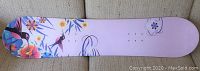 Photo of snowboard base showing pink background with floral and hummingbird designs