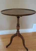 Full view of vintage solid wood circular table with tripod legs on hardwood floor.