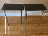 Two black textured top folding TV trays with chrome legs, viewed front-on