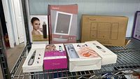 Photo of all boxed items together on a metal shelf including vanity mirror, nail care set, blackhead vacuums, makeup mirror, massager pen
