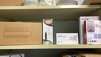 Photo showing boxed Geryon vacuum sealer, Fkant milk frother box, and electronic alarm clock on shelf.