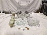 Full lot showing 2 clear glass oil lanterns, 3 floral-patterned teacups, Lalique fish figurine, 2 pineapple glass bowls, and a Haviland vase on white cloth background