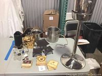 Photo showing various wine accessories on table, including 3 ice buckets (one standing), gold bottle holder, wine cooler, salt shakers, and coasters at front.