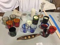Group photo showing 3 amber and red colored Carlo Moretti glass candle holders, 2 Bormioli glass candle holders, 4 Celebrate It candle holders (blue, green, black, and red), a wooden carved canoe-shaped holder with 3 candles, and several pillar candles