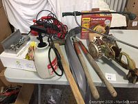 General overview of tools and garden equipment on table including paint eater, axe, shears, sprayer and walking sprinkler