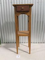 Front view of an antique wooden pedestal table showing drawer and lower shelf.