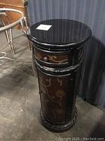 Full view of the pedestal table showing round top, drawer, cabinet door with floral painted designs and carved base.