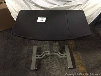 Image shows adjustable work table from front view with dark tabletop and metal frame on wheels.