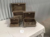 Three nesting wooden boxes with lids open showing interior, displaying carved details and size variations.