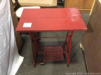 Front view of the vintage sewing table showing red painted wooden tabletop and metal base with treadle.