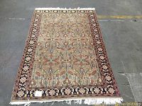 Full view of rectangular patterned rug with floral and geometric design. Rug shown on floor with some fringe missing.