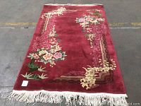 Full view of burgundy floral rug showing overall pattern and fringes at one end.