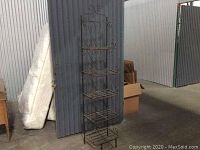 Full view of the tall metal baker's rack against a corrugated metal wall, showing all five shelves and the open wire-frame design.
