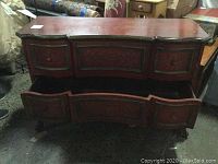 Full view of the front of the burgundy dresser showing its carved wooden legs, curved front panels, and two open drawers.