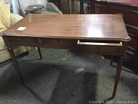 Full view of antique wooden desk showing rectangular top, three drawers, carved edges, and tapered legs.