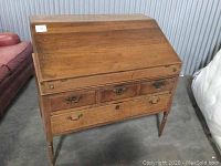 Front view of the closed desk showing the drop-front surface and four drawers below.