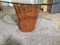 Close up of the wooden pedestal base resembling a tree trunk with natural wood grain detail beneath the clear glass top.
