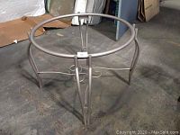 Full view of metal round table base without glass top, showing circular ring and curved legs.
