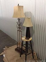 Pair of lamps shown side by side, floor lamp with metal scroll base and suede shade, table lamp on stool with suede shade