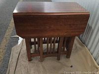 Front view of the antique drop leaf table in closed position showing the wooden tabletop and leg structure.