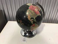 Front view of a black and red vintage decorative globe on a shiny silver metal base, showing North America prominently.