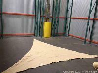 Photo showing large triangular nude-colored shade sail spread out on warehouse floor, illustrating size and shape.