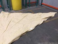 Large nude triangular shade sail fabric spread on concrete floor inside a warehouse.
