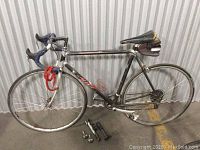 Side profile of black and silver road bike with blue wrapped handlebar tape. Two pumps and metal items are on the ground beside bike.