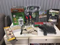 Full view of gardening tools and supplies including Flo Master sprayer, clothespins, potting hole diggers, drill bits, decorative turtle, plastic sheeting, tree staking kits, vertical planters, and gopher wire basket.