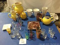 Set of pitchers, teapot, mugs, shot glasses, plates, and glassware arranged on blue surface.