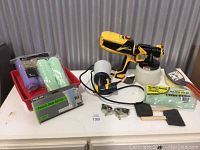 Two Wagner paint sprayers, paint tray, roller sleeves, paint pad refills, protective goggles, and brushes on white surface