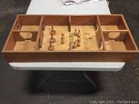 Wooden skittle board game set with multiple pins and pucks placed inside game compartments on white table.