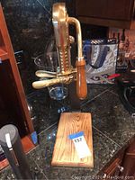Large vintage-style decorative manual wine bottle opener mounted on wooden base, showing gold-tone metal and wooden handle on granite countertop